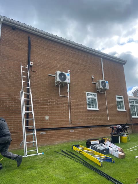 Engineers installing two air conditioning outdoor units on the side of a building using ladders