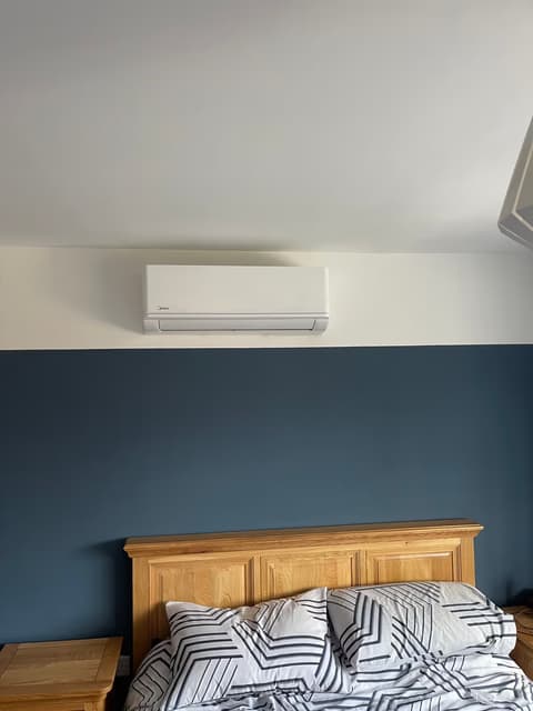 Wall-mounted bedroom air conditioning unit installed on a dark blue feature wall above the bed