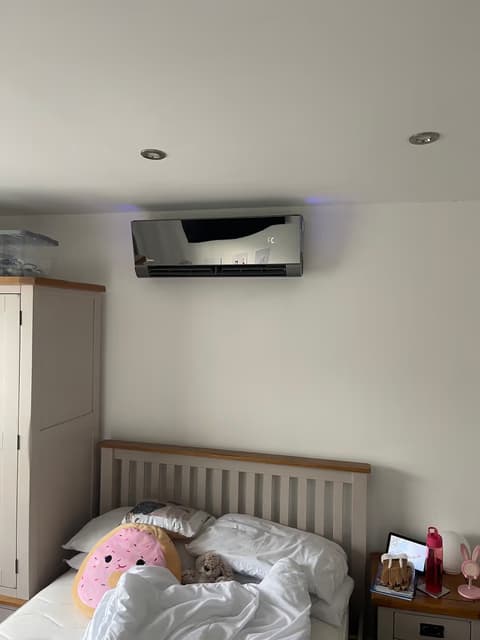 Black mirror-finish wall-mounted air conditioner installed above a bed in a bedroom