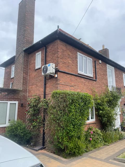 Air conditioning outdoor unit fitted to the side wall of a 1930s-style brick house