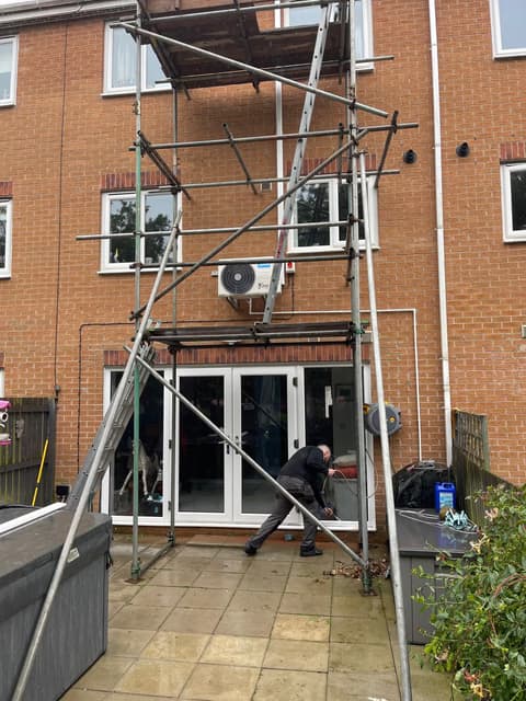 Air conditioning engineer installing outdoor units from scaffolding on a brick house