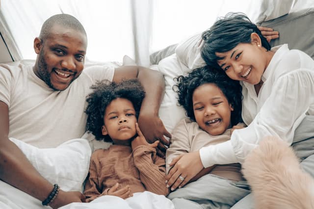 Family relaxing together on a bed in a cool, comfortable bedroom