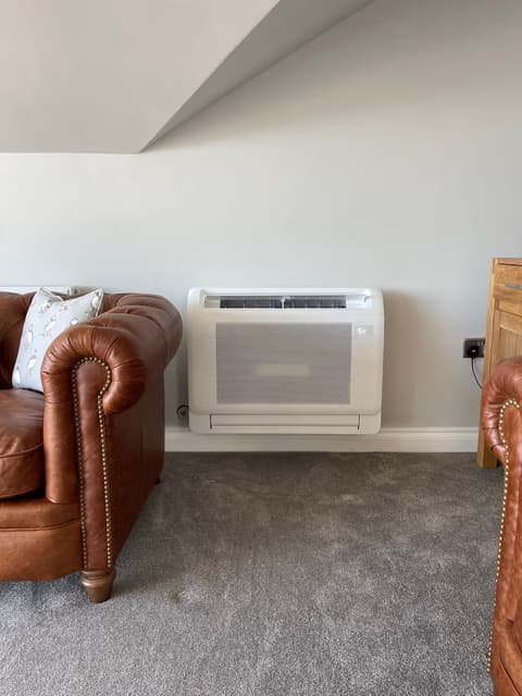 White floor-mounted air conditioning console beside a leather sofa in a lounge