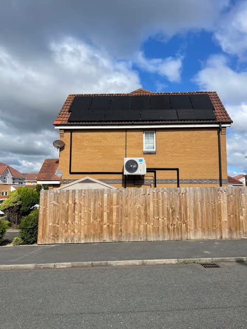 Air conditioning outdoor unit on a new-build house with solar panels on the roof