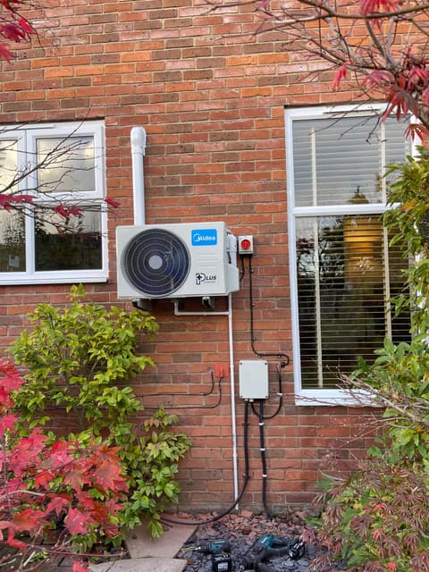 Split system outdoor condenser unit mounted on a brick wall next to a window