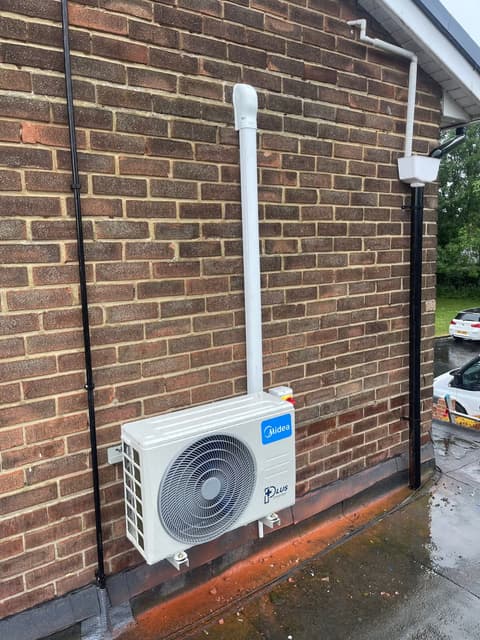 Air conditioning outdoor unit with pipework trunking running up an exterior brick wall