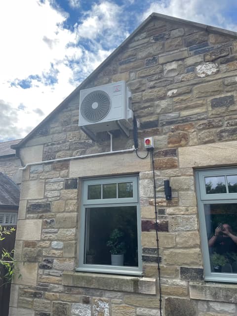 Air conditioning outdoor unit discreetly mounted on the gable of a stone cottage