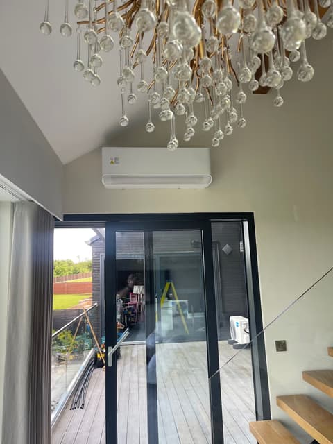 Wall-mounted air conditioner in a vaulted extension with black bi-fold doors and a chandelier